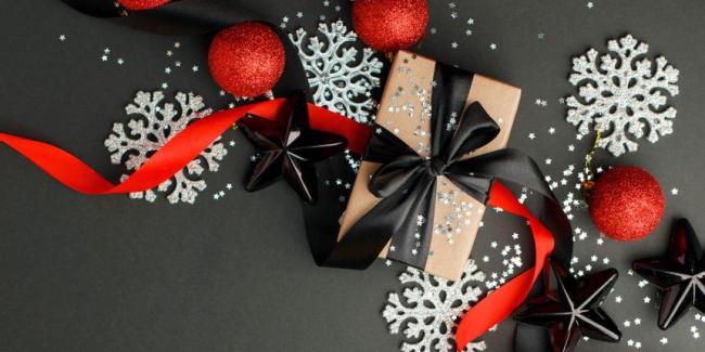 Red and Black Round tree ornaments, ribbon, and white snowflakes on a grey background.